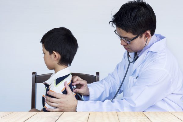 Sick asian boy being examined by male doctor over white background